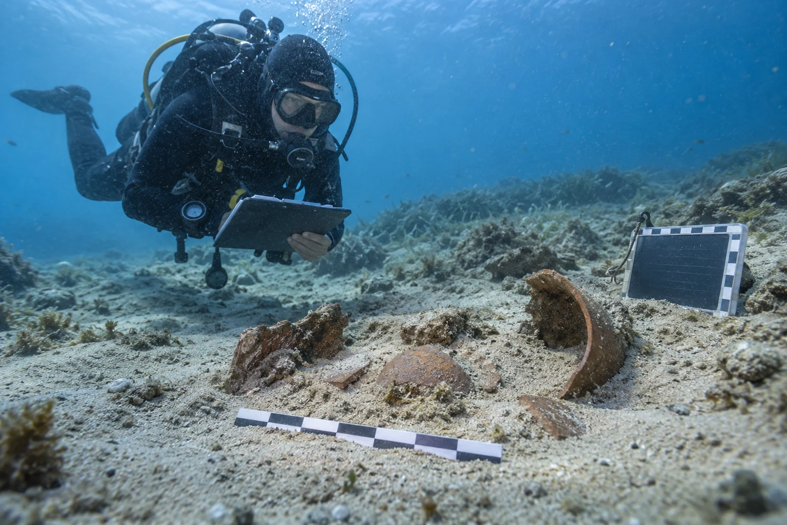 Ein Unterwasserarchäologe dokumentiert Keramikfragmente über sandigem Meeresboden, ohne sie zu berühren
